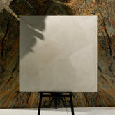 Crema Onyx glossy porcelain tile 120x120cm on easel against luxury marble backdrop showing cream and gold veining for UAE interiors